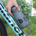 Metal bike water bottle cage holding a dark gray bottle on a turquoise frame